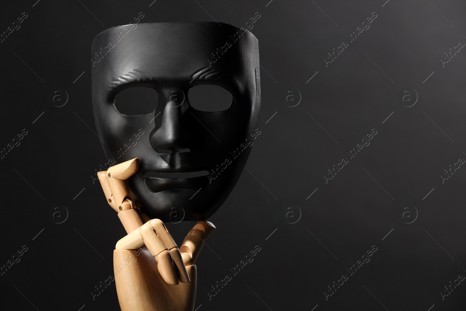 Photo of Wooden mannequin hand holding plastic mask on black background, space for text. Theatrical performance