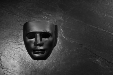 Plastic face mask on black slate surface, top view and space for text. Theatrical performance