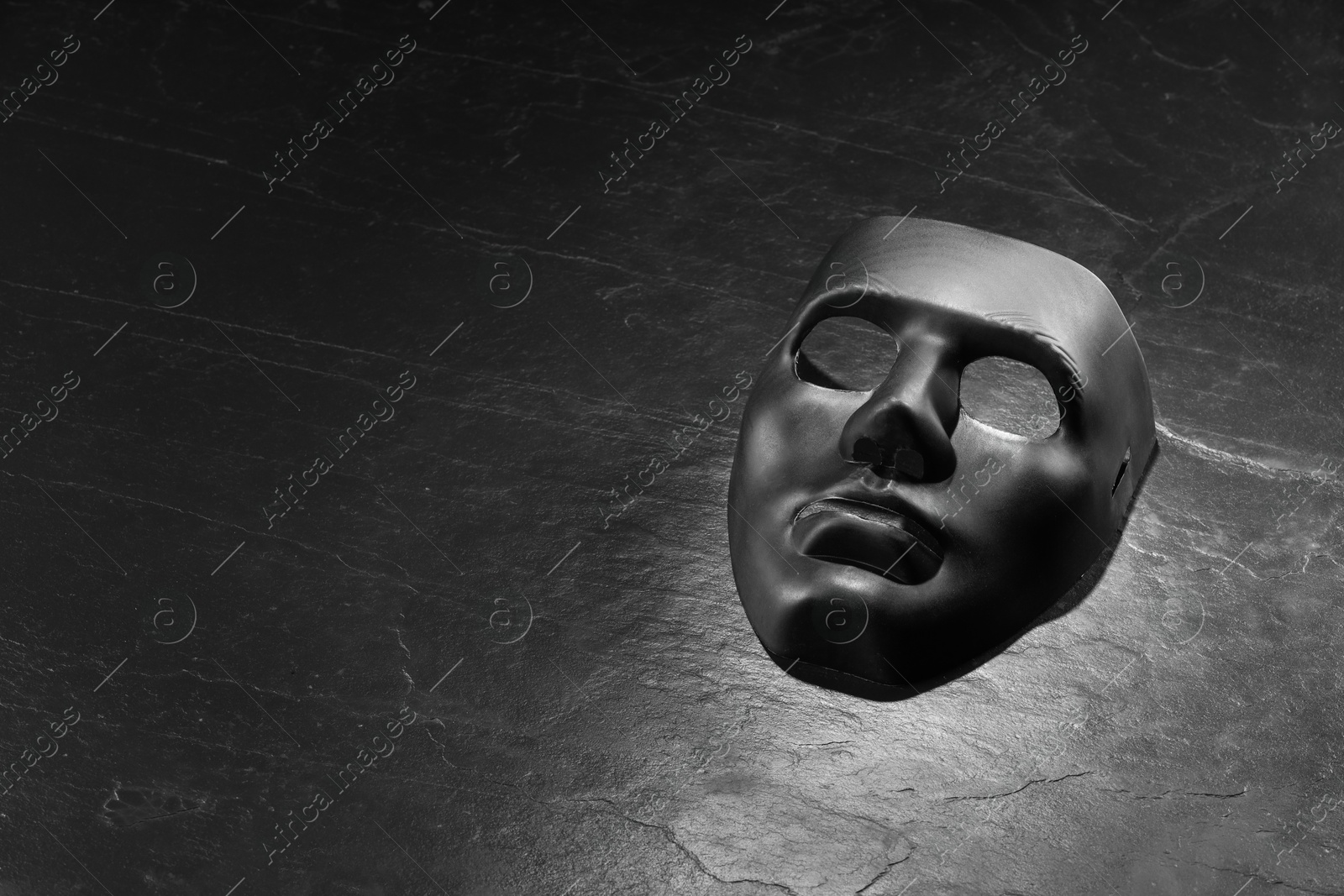 Photo of Plastic face mask on black slate surface, space for text. Theatrical performance