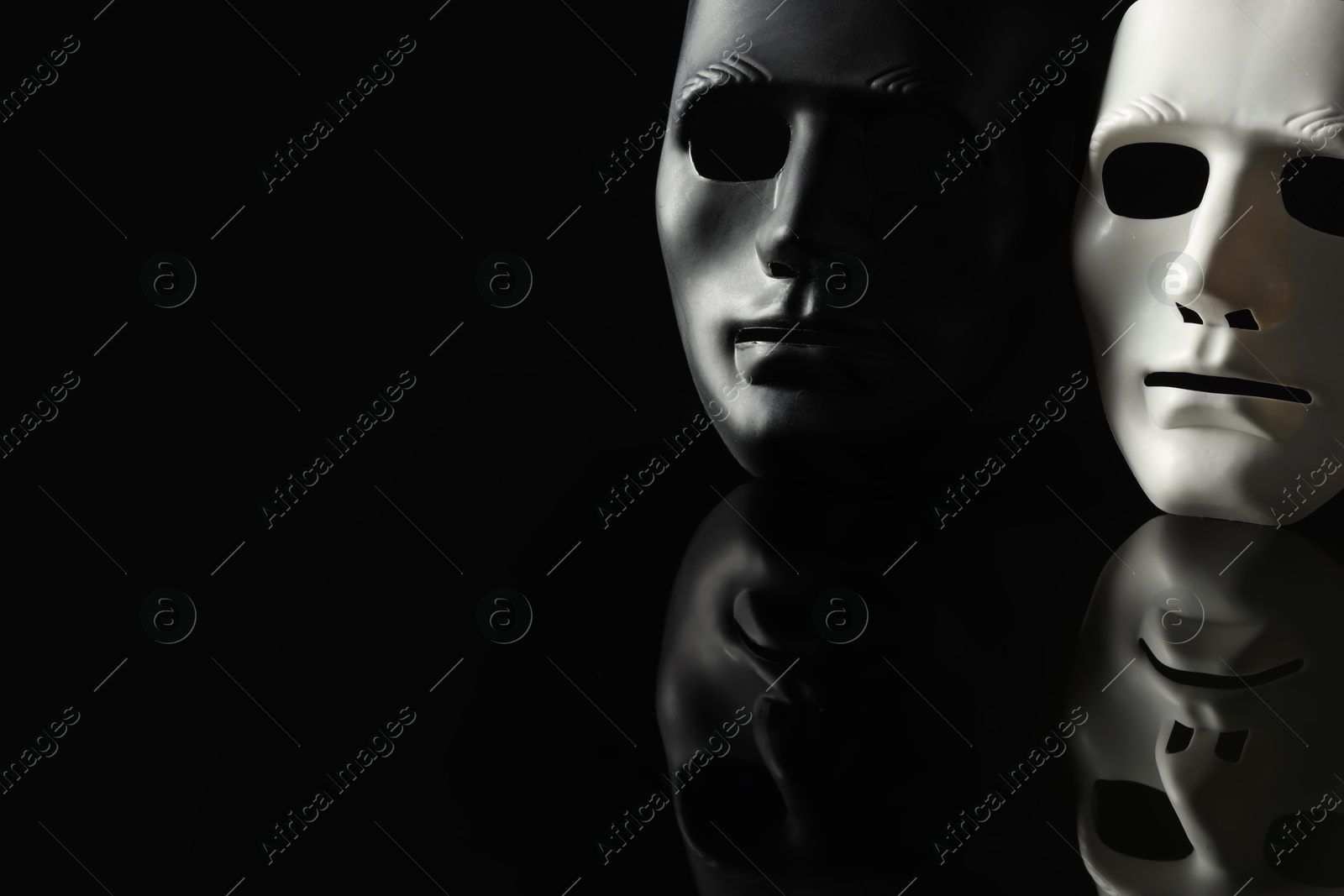 Photo of Plastic face masks on black mirror surface, space for text. Theatrical performance