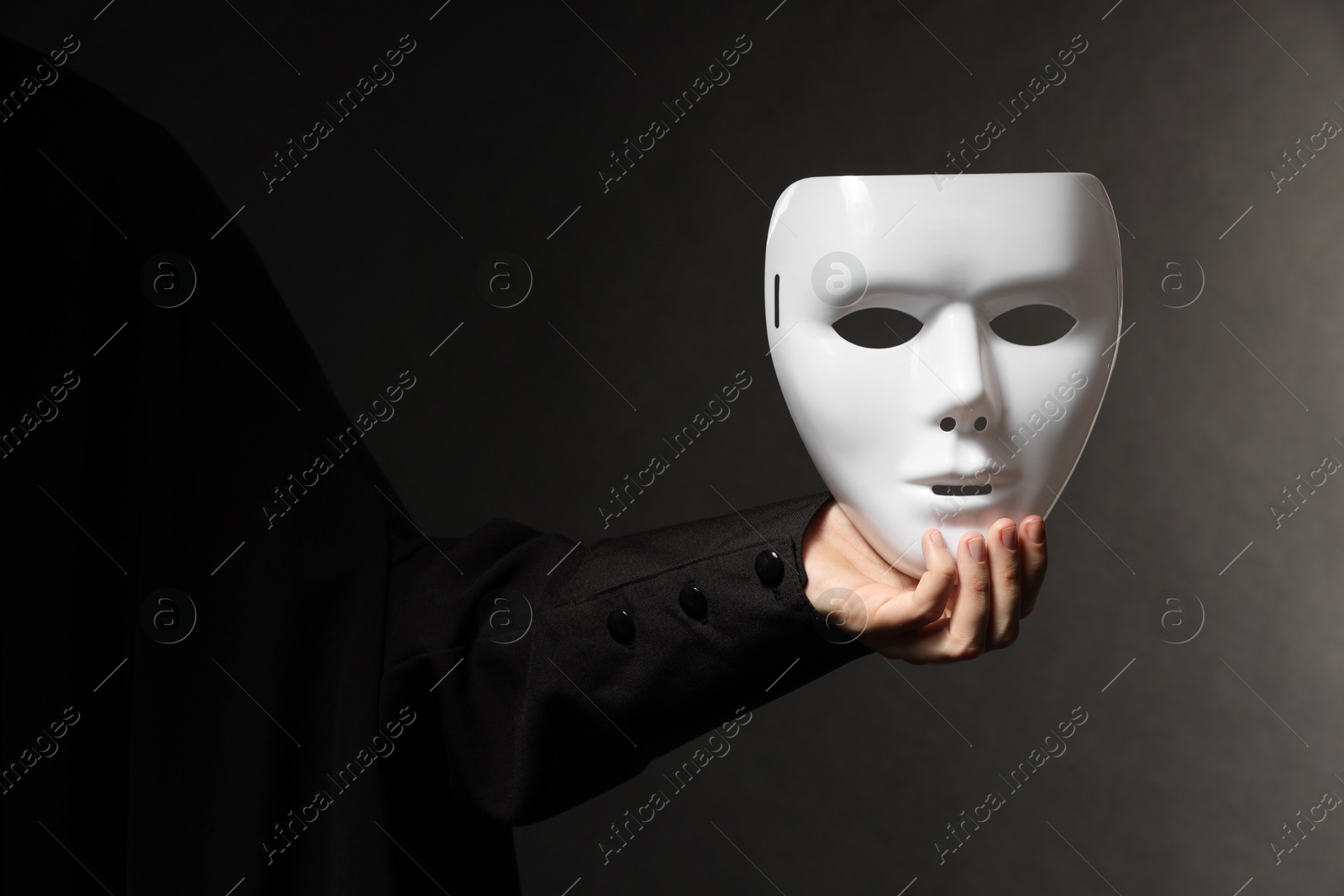 Photo of Theatrical performance. Man holding plastic mask on black background, closeup