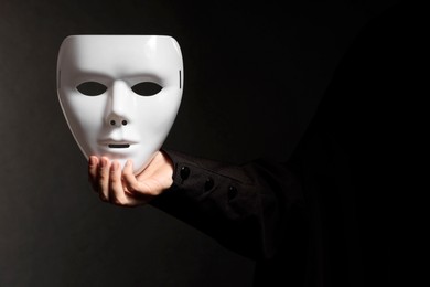 Photo of Theatrical performance. Man holding plastic mask on black background, closeup