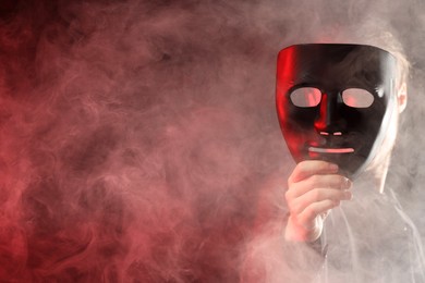 Theatrical performance. Man with plastic mask in smoke on dark background, space for text