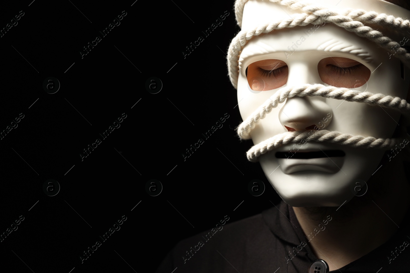 Photo of Theatrical performance. Man with plastic mask and hemp rope on black background, space for text