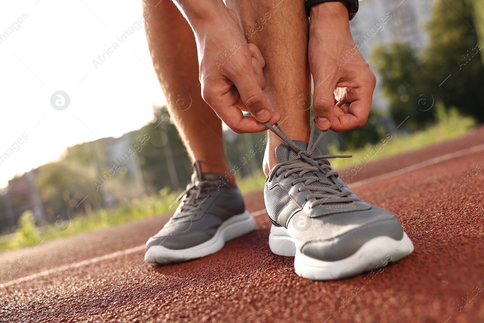 Photo of Man tying shoelace of grey sneaker at stadium, closeup