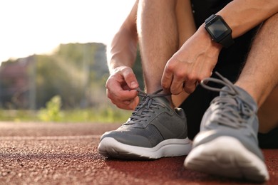 Photo of Man tying shoelace of grey sneaker at stadium, closeup. Space for text