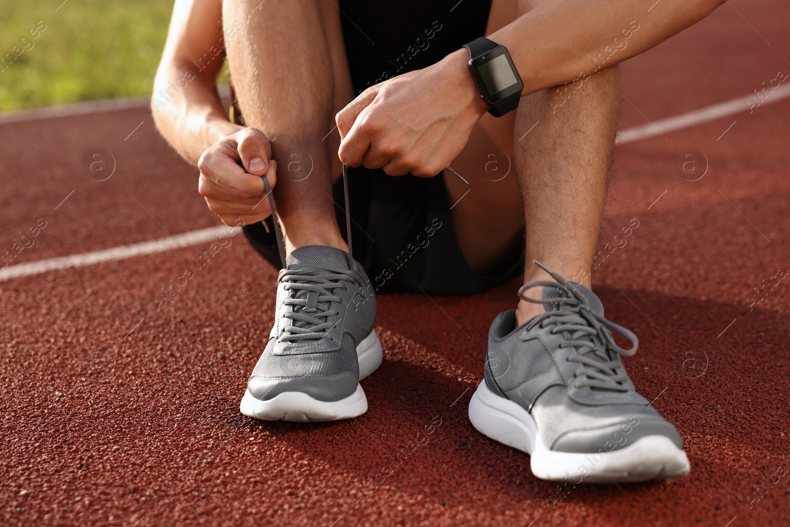 Photo of Man tying shoelace of grey sneaker at stadium, closeup