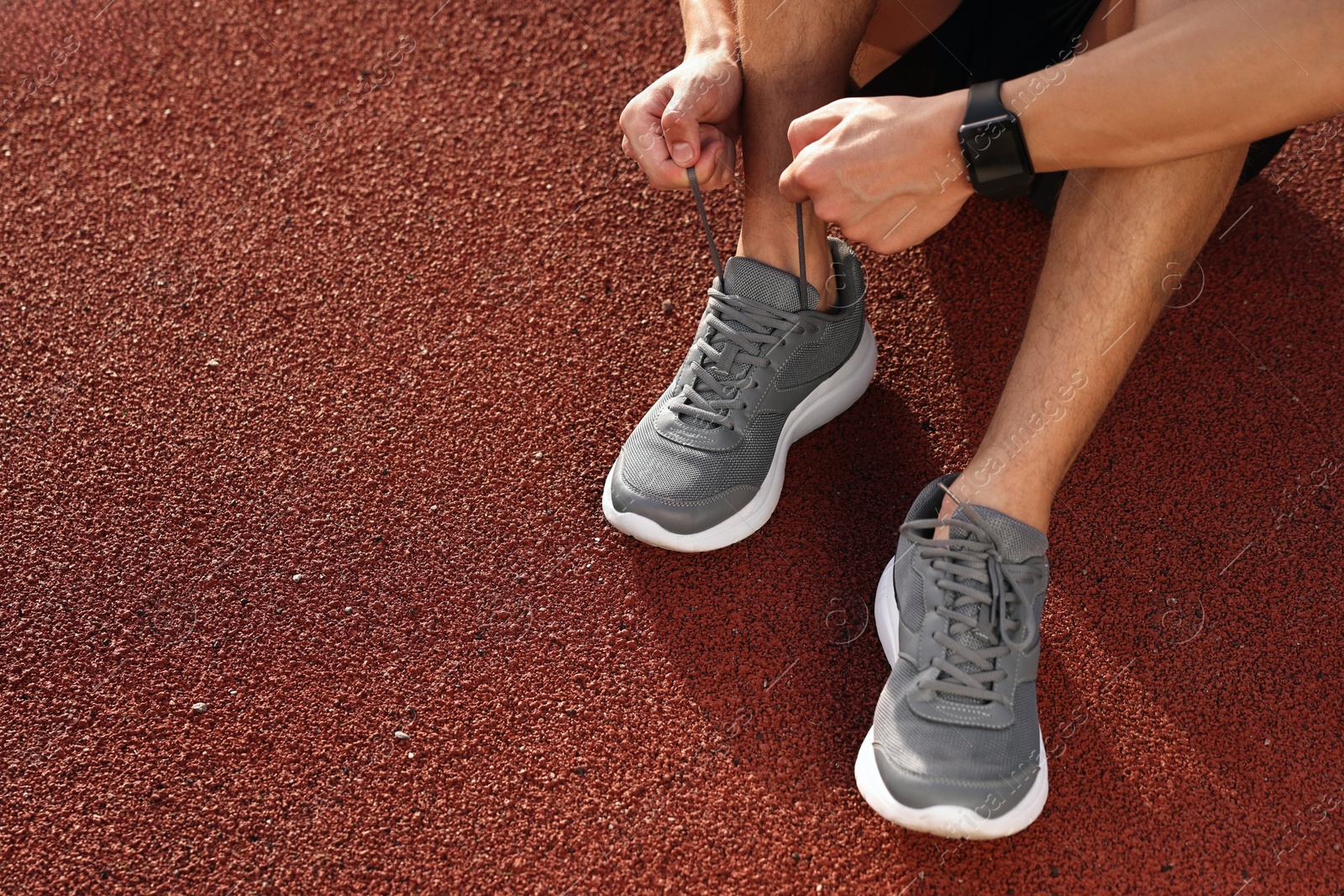 Photo of Man tying shoelace of grey sneaker at stadium, closeup. Space for text