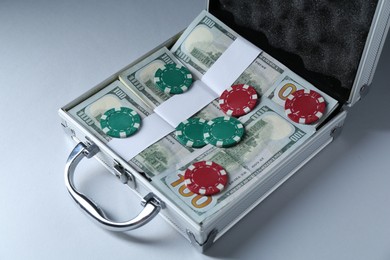 Photo of Metal case full of dollar banknotes and casino chips on light background