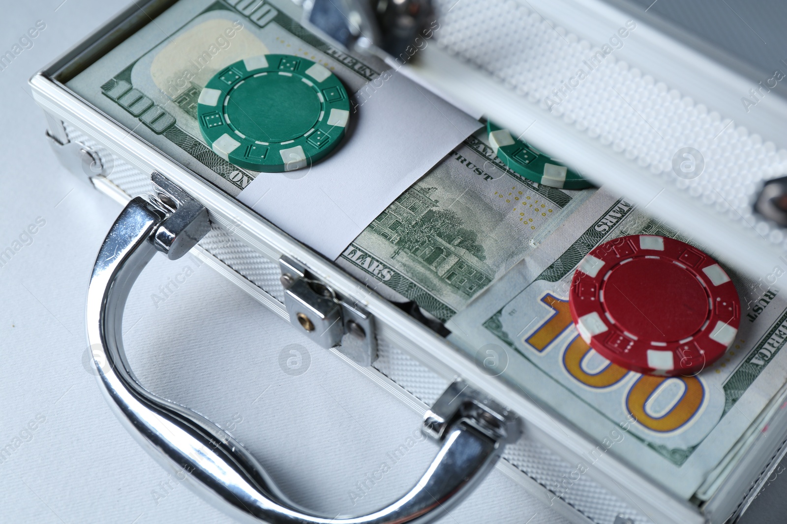 Photo of Metal case full of dollar banknotes and casino chips on light background, closeup