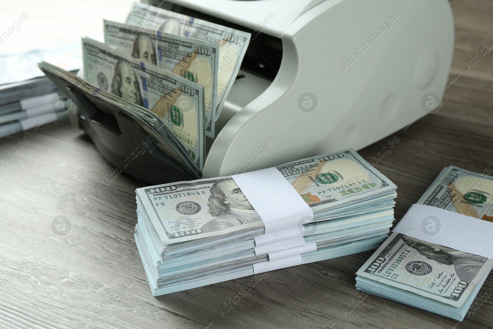 Photo of Money counter machine with dollar banknotes on wooden table, closeup