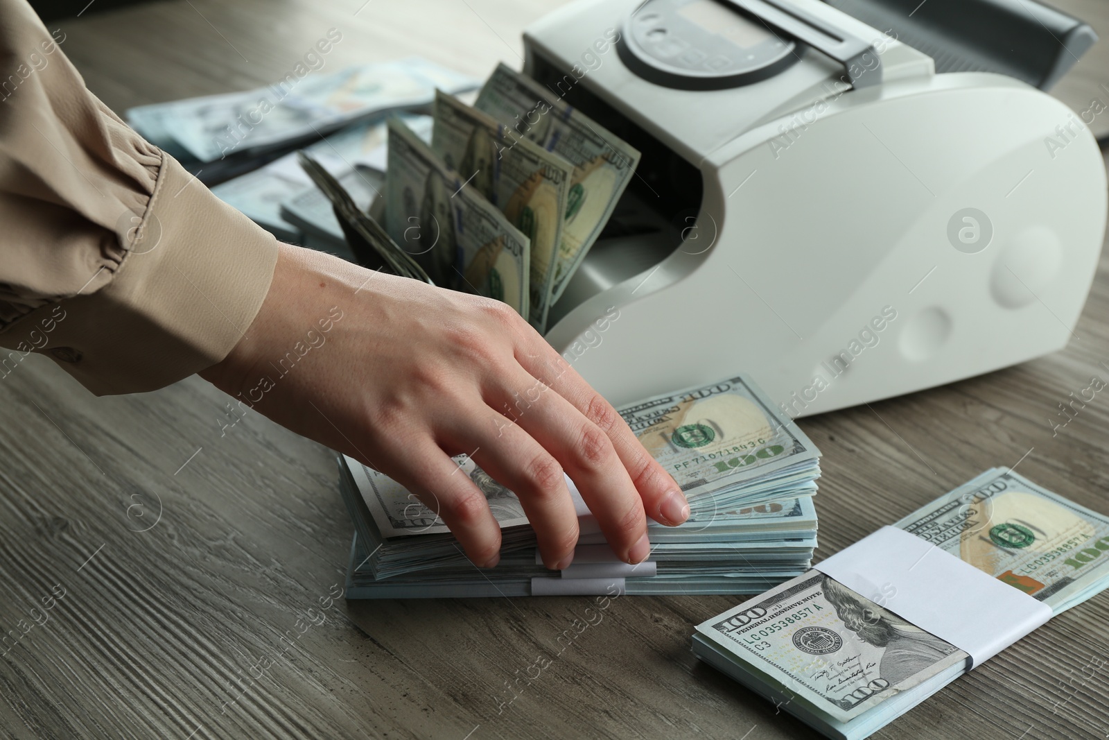 Photo of Woman using money counter machine at wooden table, closeup