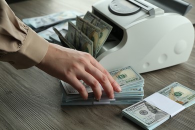 Woman using money counter machine at wooden table, closeup