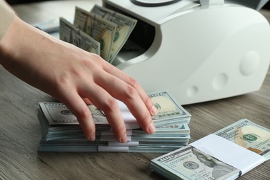 Woman using money counter machine at wooden table, closeup