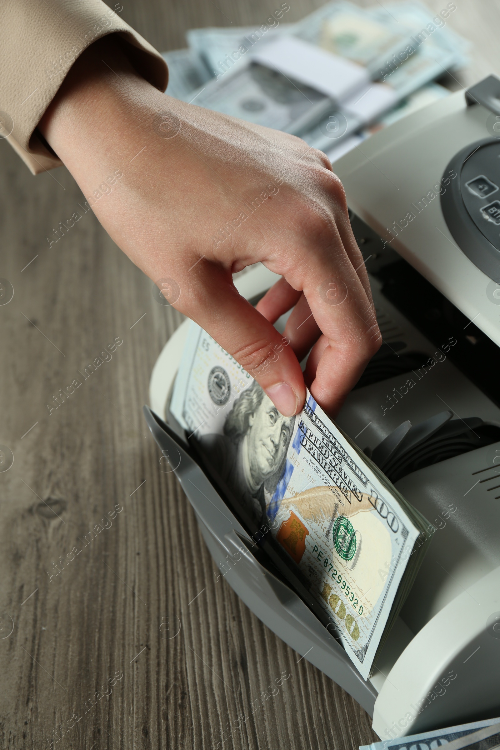 Photo of Woman using money counter machine at wooden table, closeup