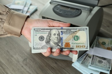 Woman with dollar banknotes near money counter machine at wooden table, closeup