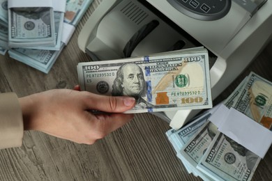 Woman using money counter machine at wooden table, closeup