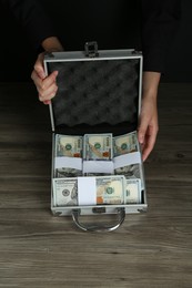 Photo of Woman with metal case full of dollar banknotes at wooden table, closeup