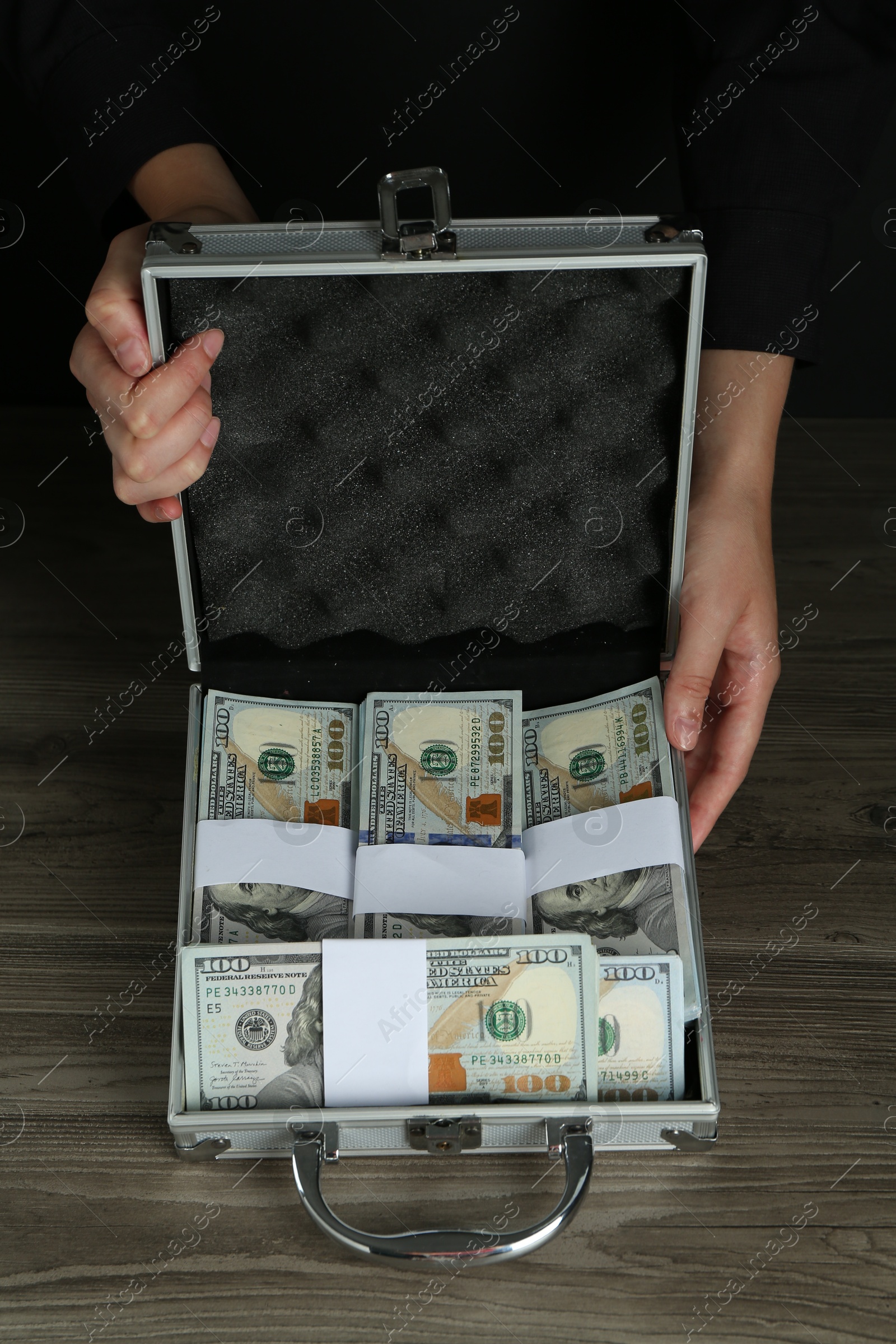 Photo of Woman with metal case full of dollar banknotes at wooden table, closeup