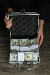 Woman with metal case full of dollar banknotes at wooden table, closeup