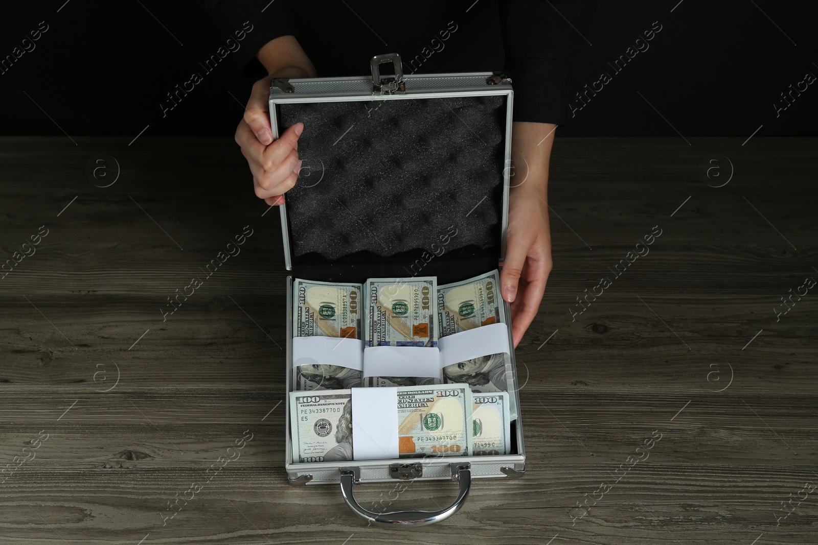 Photo of Woman with metal case full of dollar banknotes at wooden table, closeup