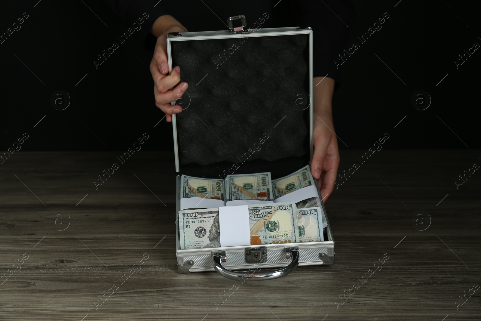 Photo of Woman with metal case full of dollar banknotes at wooden table, closeup