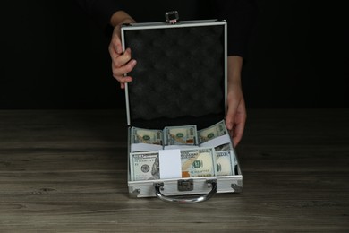 Woman with metal case full of dollar banknotes at wooden table, closeup