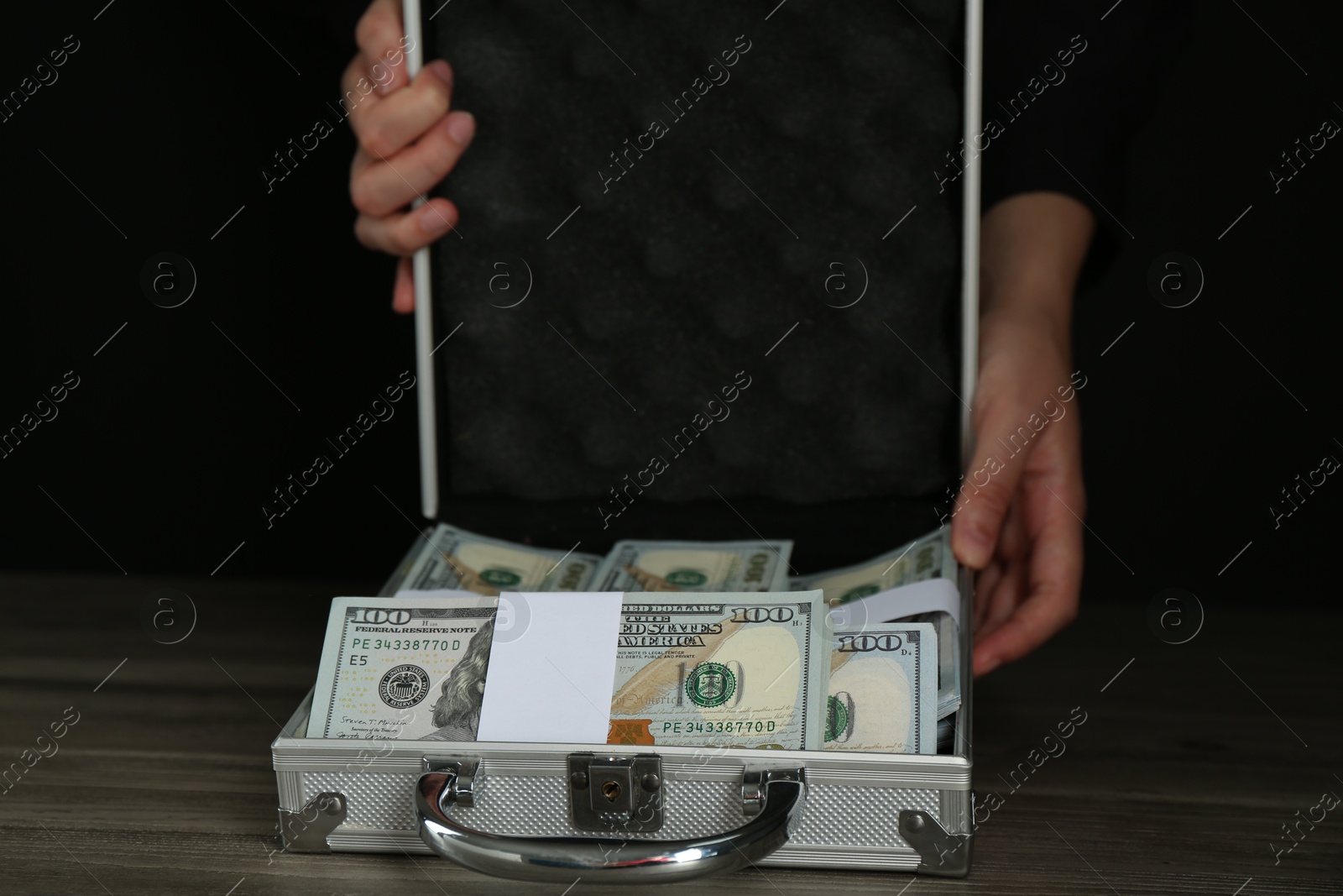 Photo of Woman with metal case full of dollar banknotes at wooden table, closeup