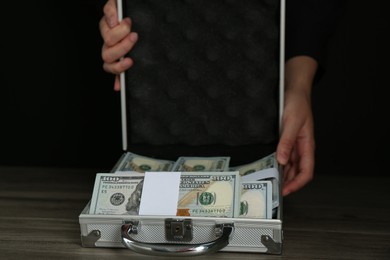 Woman with metal case full of dollar banknotes at wooden table, closeup