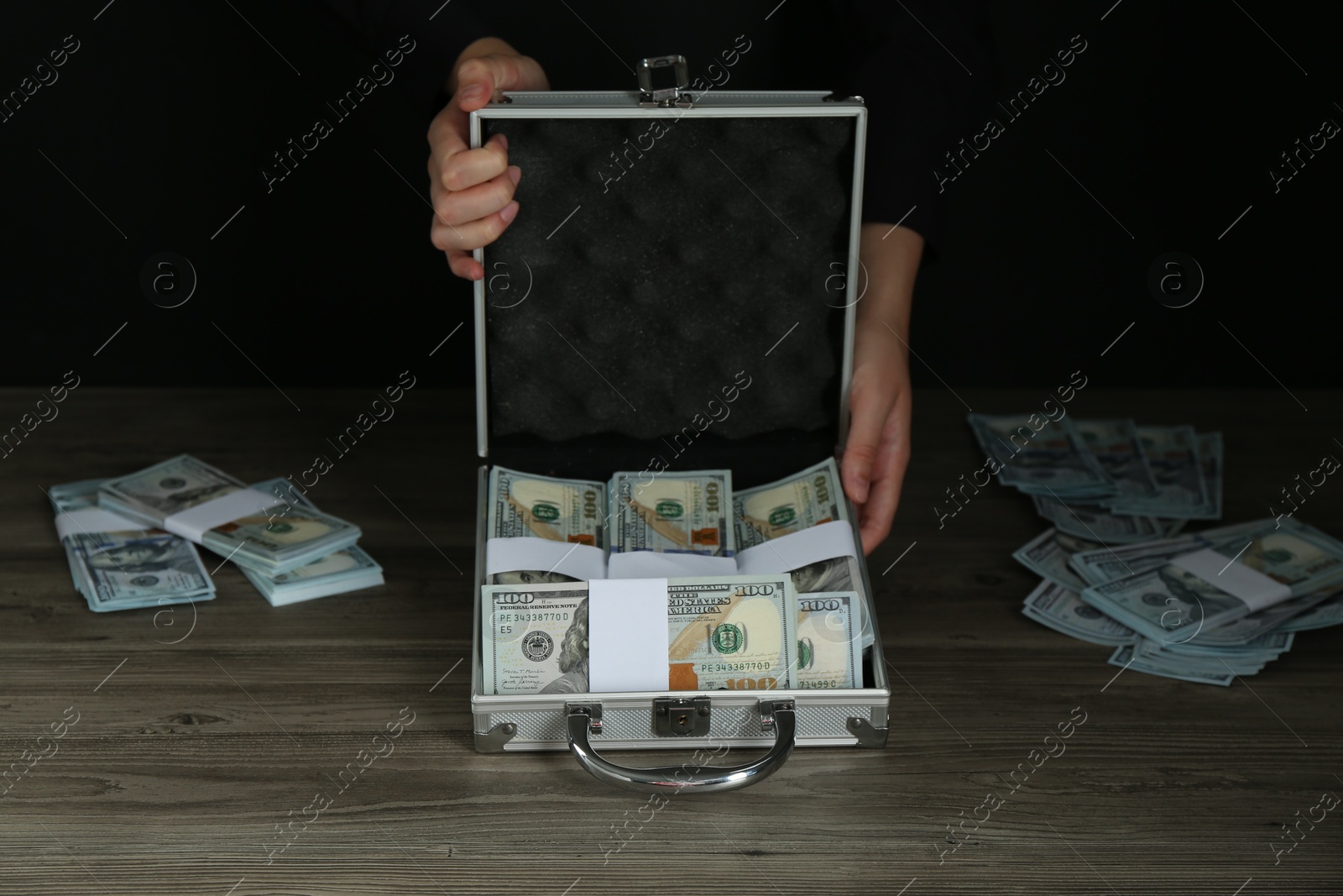 Photo of Woman with metal case full of dollar banknotes at wooden table, closeup