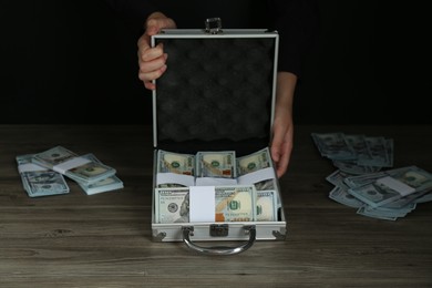 Photo of Woman with metal case full of dollar banknotes at wooden table, closeup