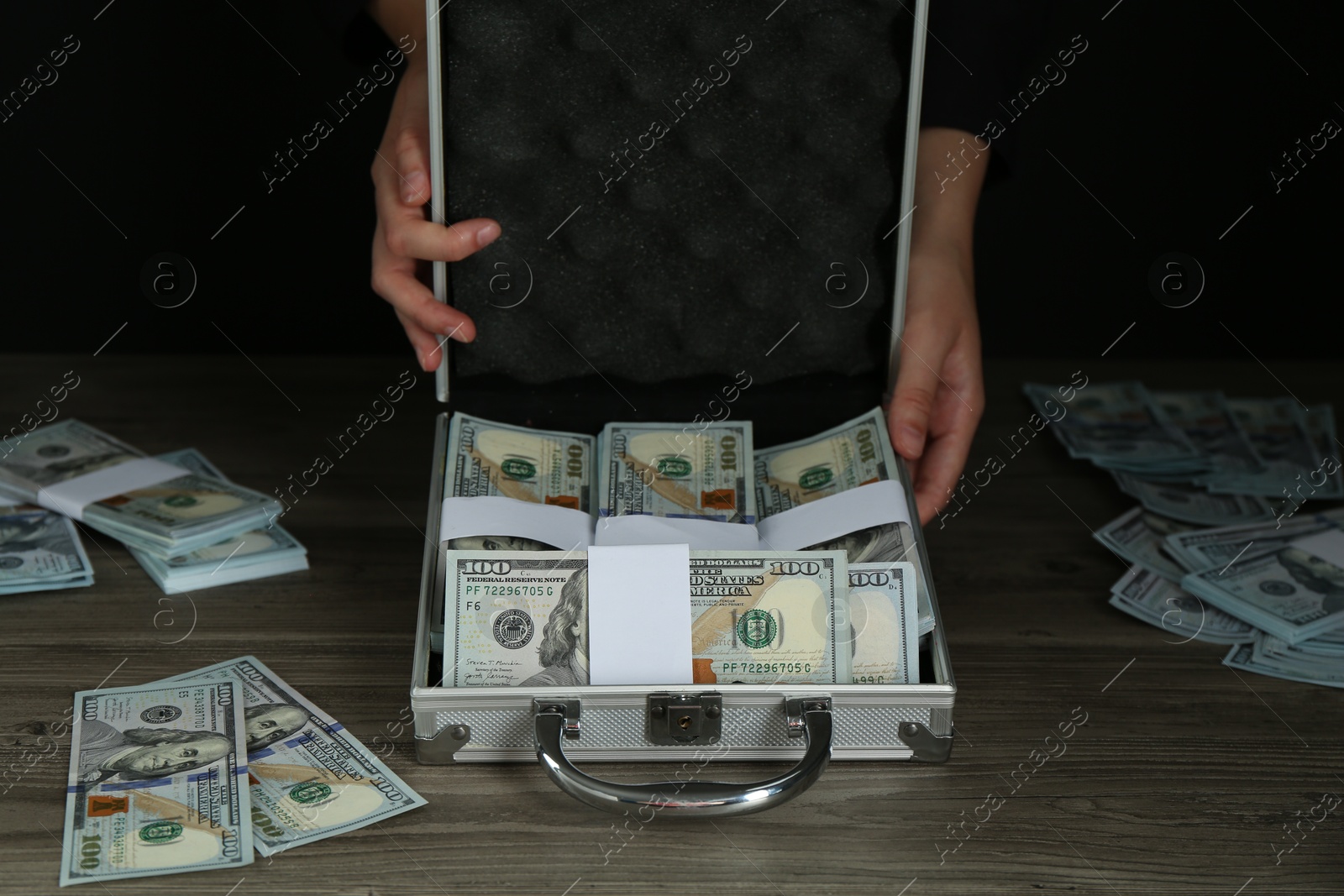 Photo of Woman with metal case full of dollar banknotes at wooden table, closeup