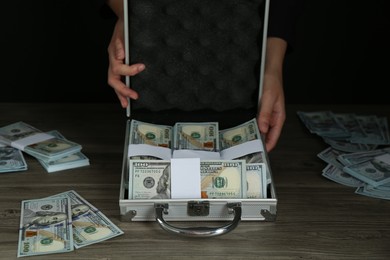 Woman with metal case full of dollar banknotes at wooden table, closeup