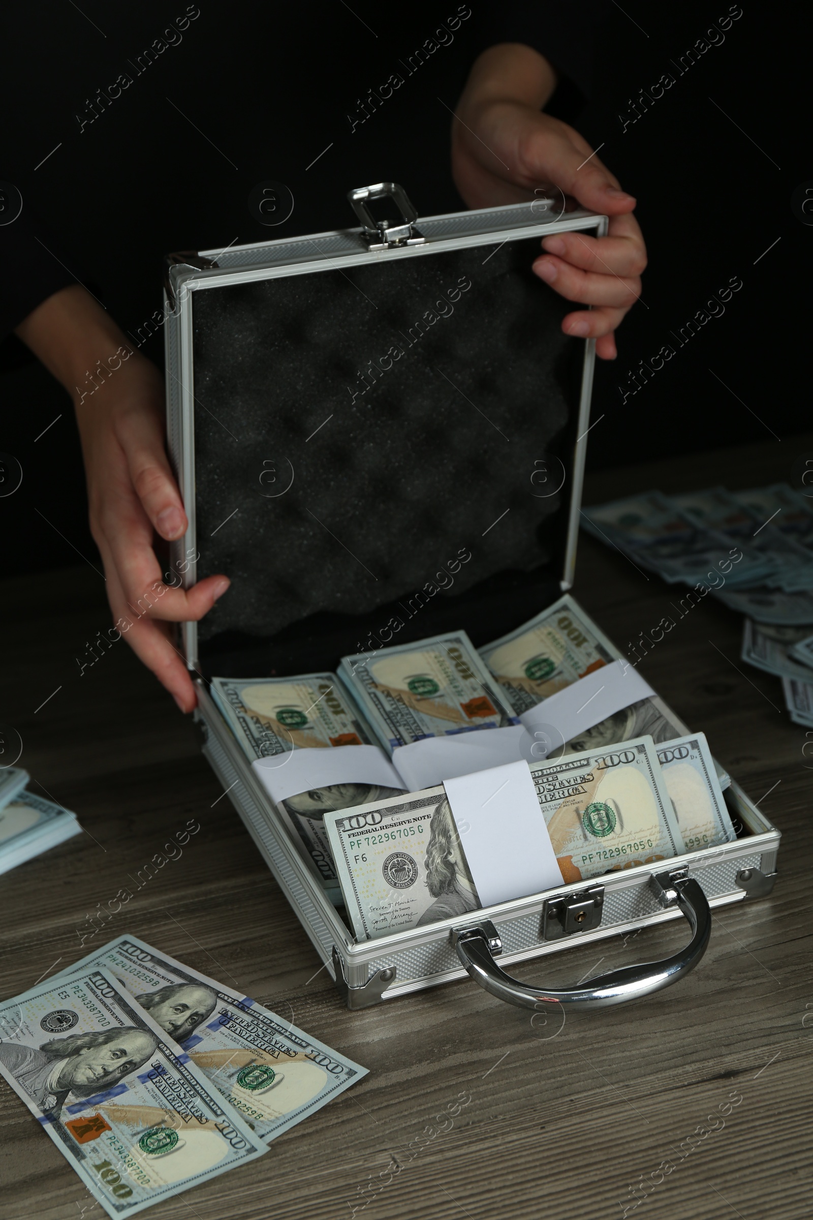 Photo of Woman with metal case full of dollar banknotes at wooden table, closeup