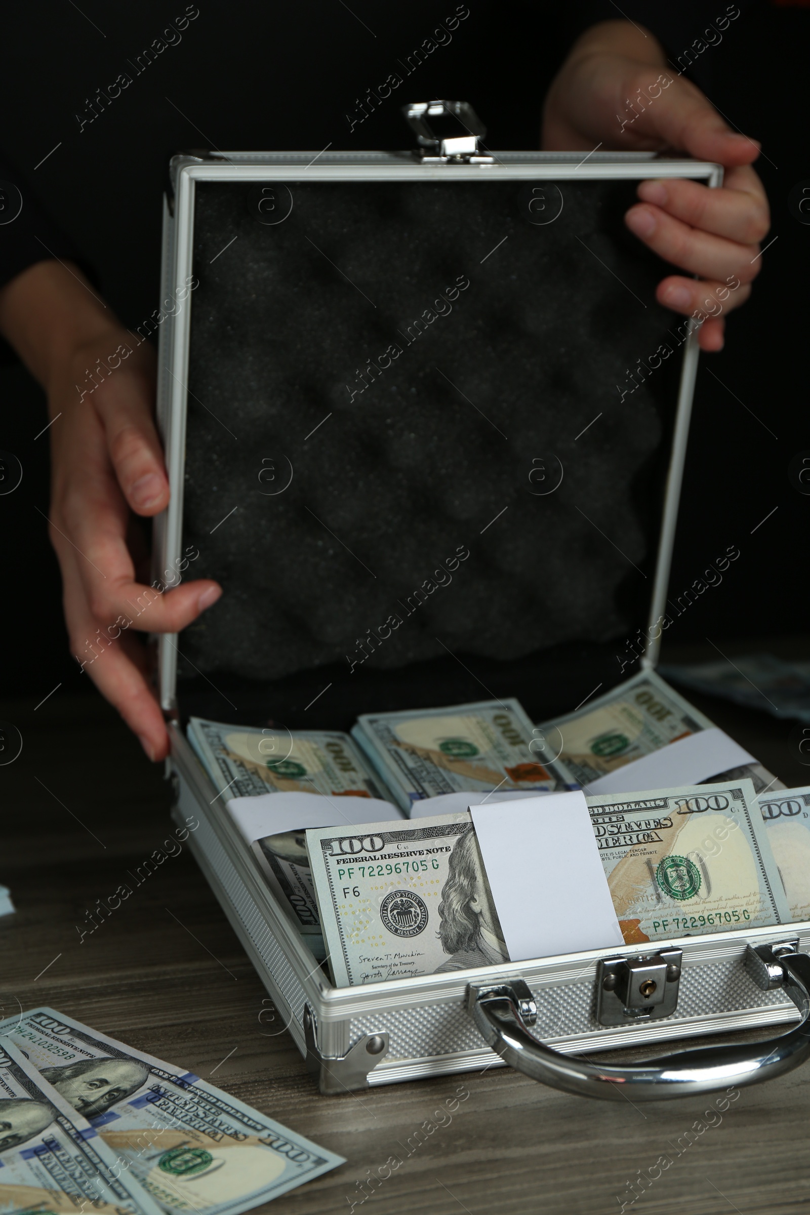 Photo of Woman with metal case full of dollar banknotes at wooden table, closeup