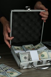 Woman with metal case full of dollar banknotes at wooden table, closeup