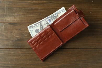 Leather wallet with dollar banknotes on wooden table, top view