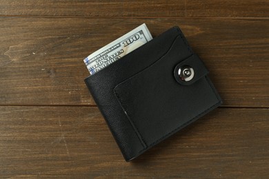 Photo of Leather wallet with dollar banknotes on wooden table, top view