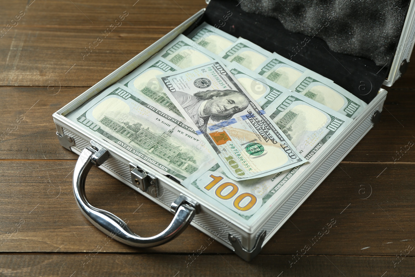 Photo of Metal case full of dollar banknotes on wooden table