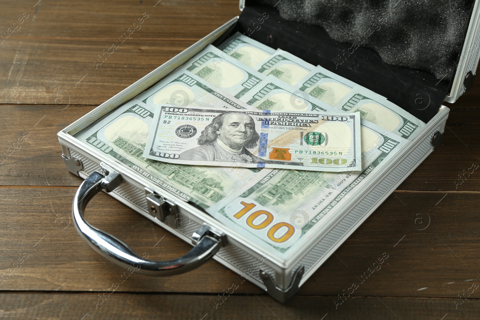 Photo of Metal case full of dollar banknotes on wooden table