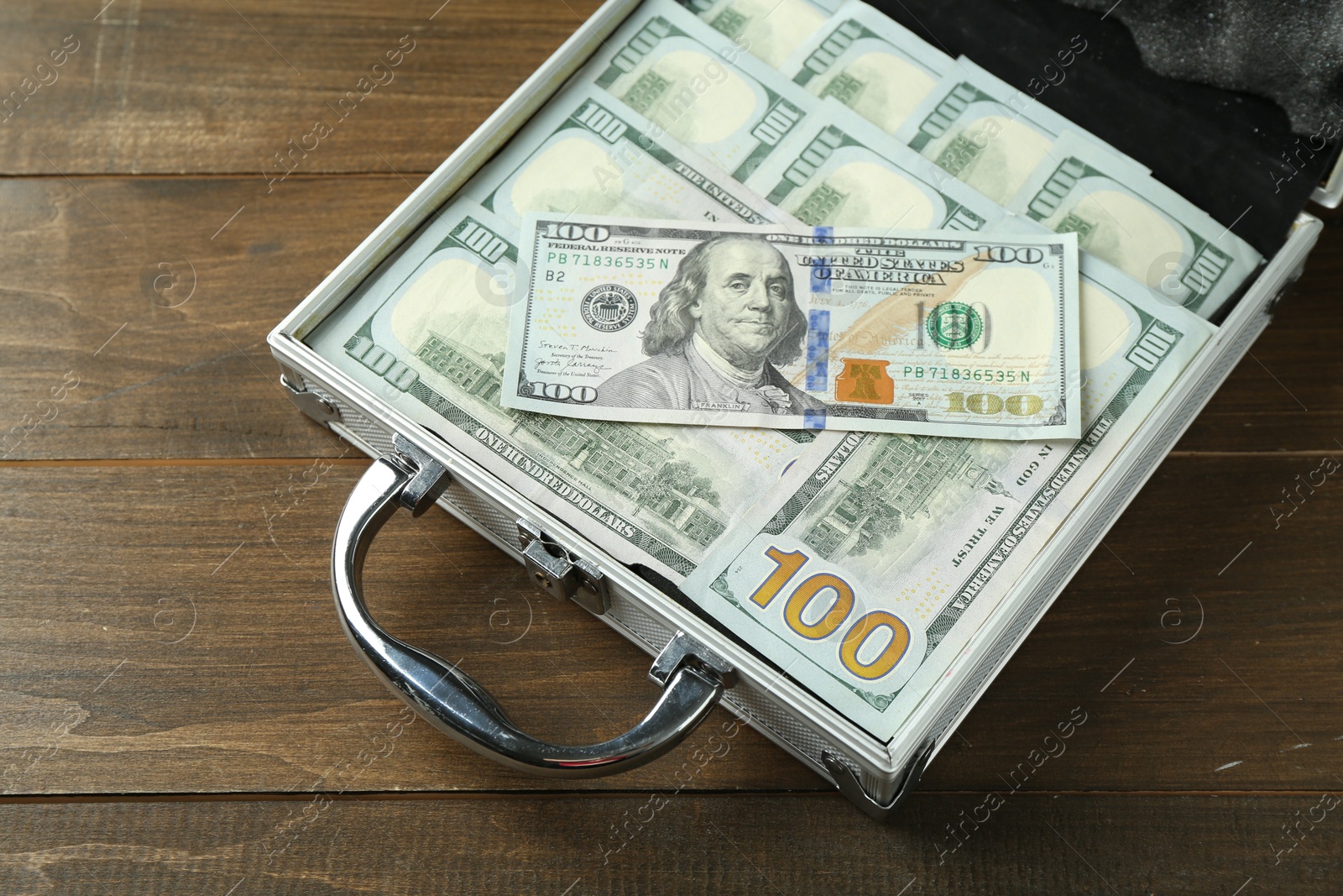 Photo of Metal case full of dollar banknotes on wooden table