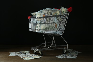 Photo of Many dollar banknotes in shopping cart on wooden table