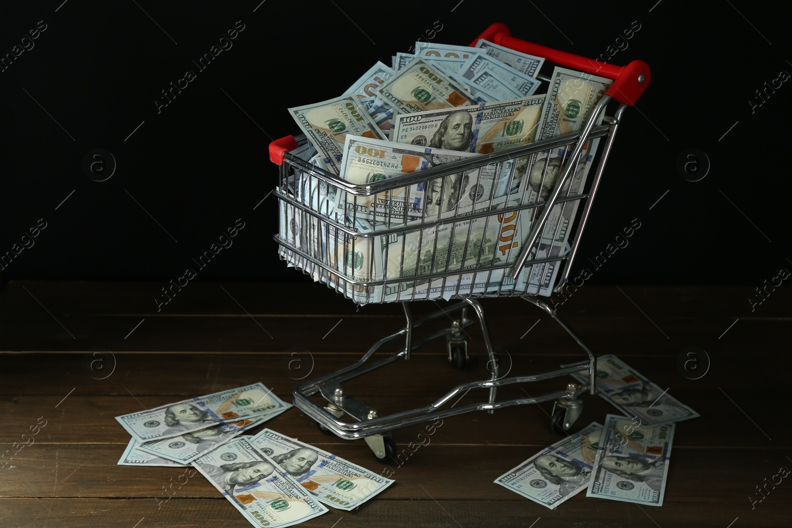 Photo of Many dollar banknotes in shopping cart on wooden table