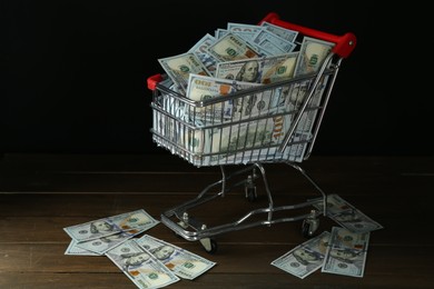 Many dollar banknotes in shopping cart on wooden table