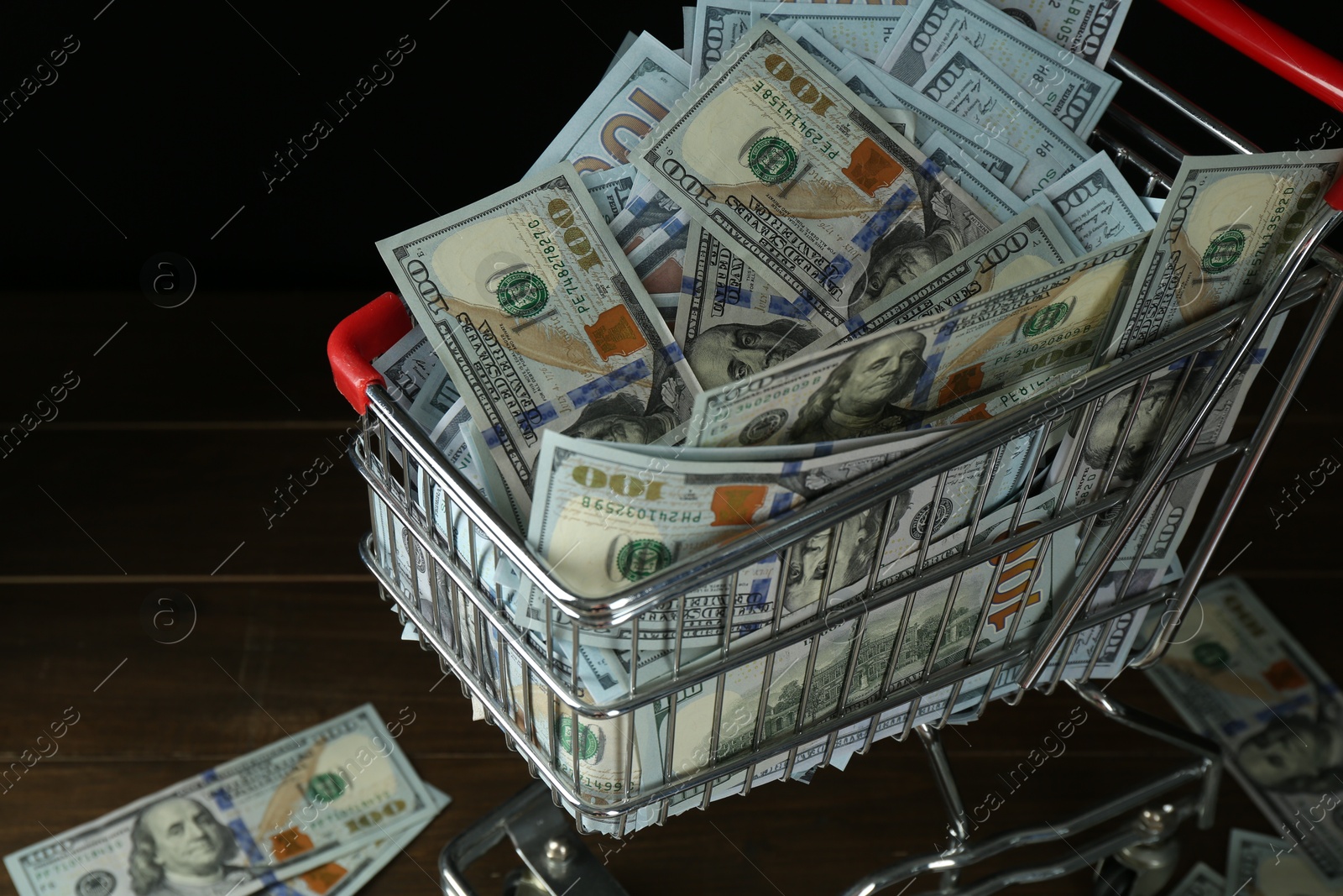 Photo of Many dollar banknotes in shopping cart on wooden table, closeup