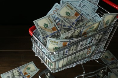 Many dollar banknotes in shopping cart on wooden table, closeup