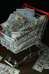 Many dollar banknotes in shopping cart on wooden table, closeup