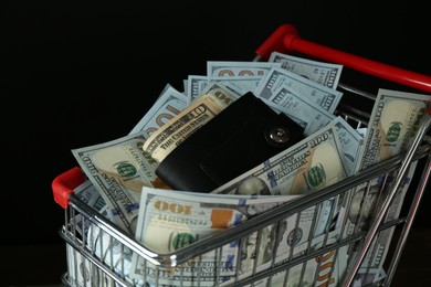 Photo of Many dollar banknotes and wallet in shopping cart on black background, closeup