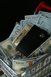 Photo of Many dollar banknotes and wallet in shopping cart on black background, closeup