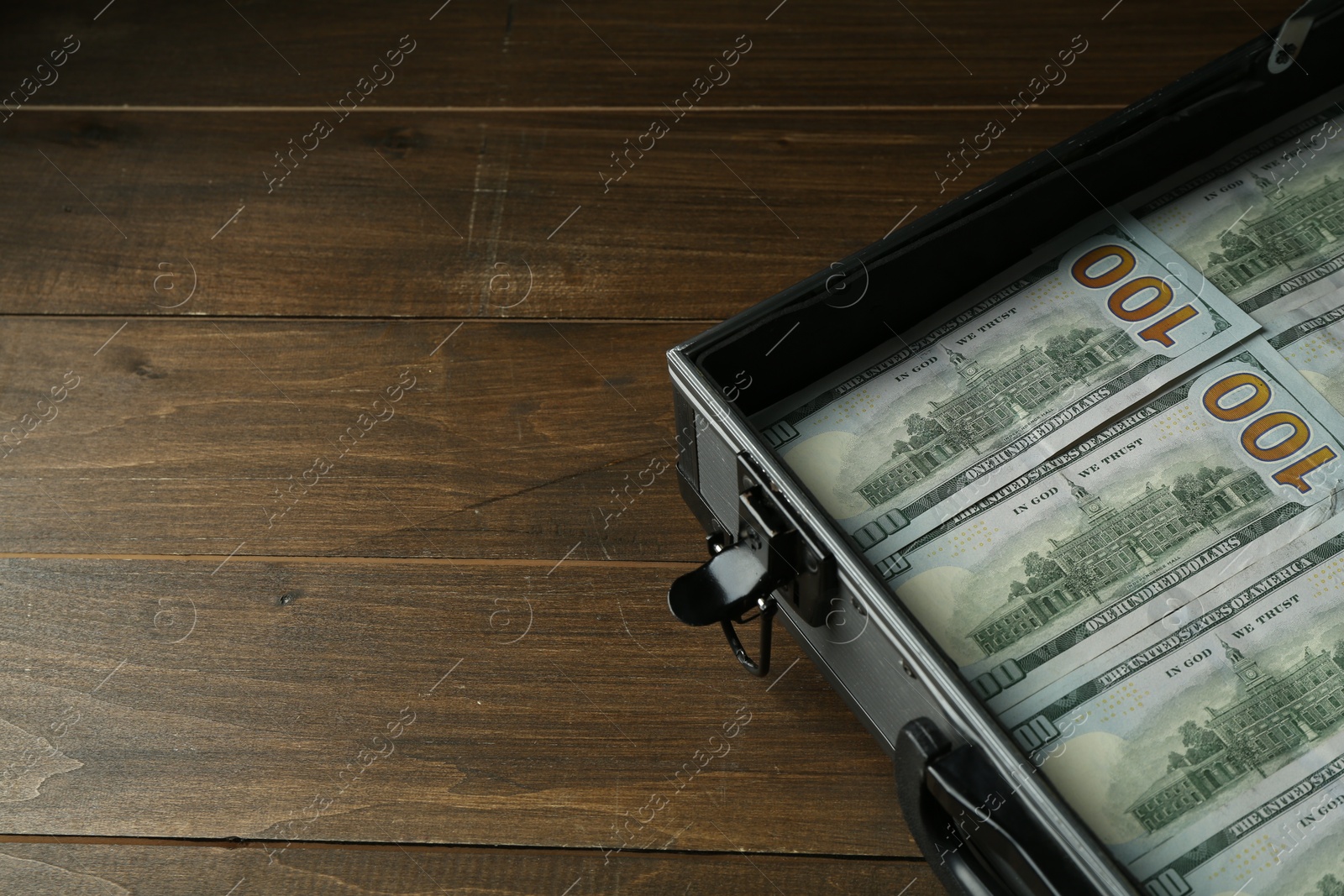 Photo of Metal case full of dollar banknotes on wooden table, space for text